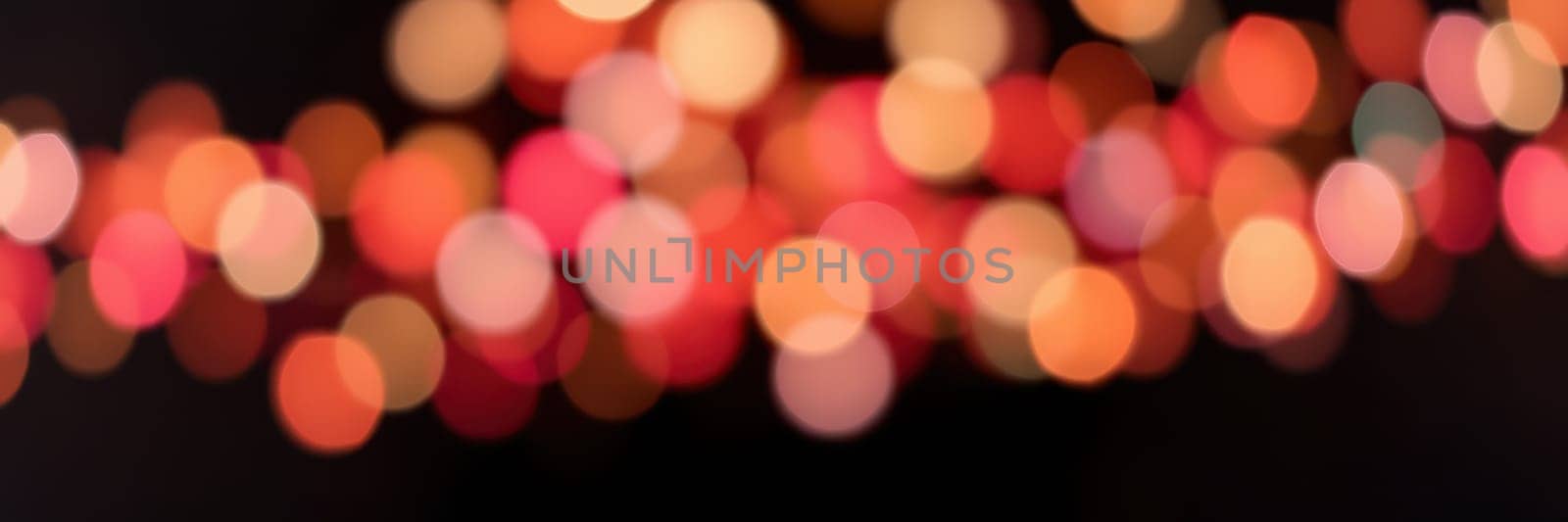 Colorful bokeh lights twinkle softly in a blurred background, enhancing the cozy and celebratory mood of an evening event. The vibrant hues of red and orange illuminate the surroundings.