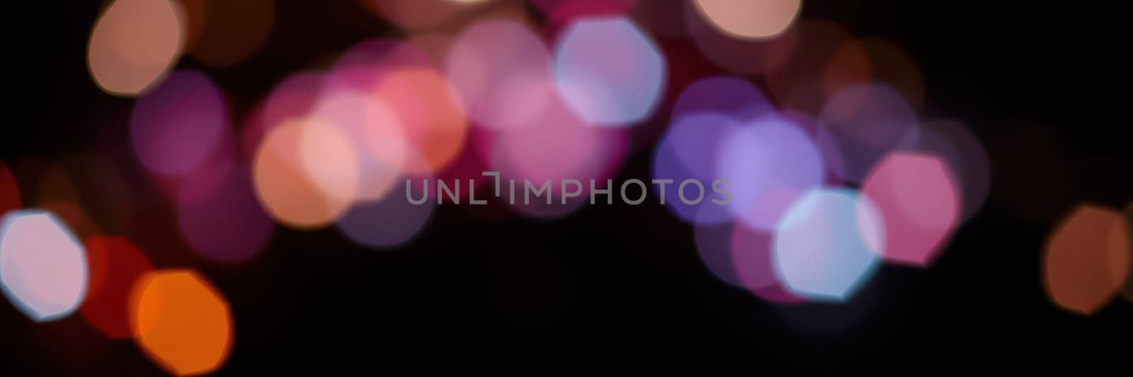 Bright, colorful bokeh lights illuminate the night, creating a lively ambiance for an outdoor celebration. The blurred lights in various hues enhance the festive mood.