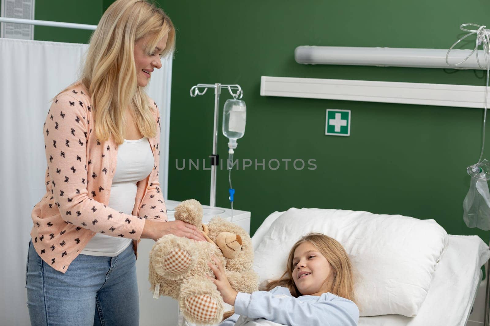 A mother comforts her sick child in a hospital room by sharing a treasured teddy bear for emotional support