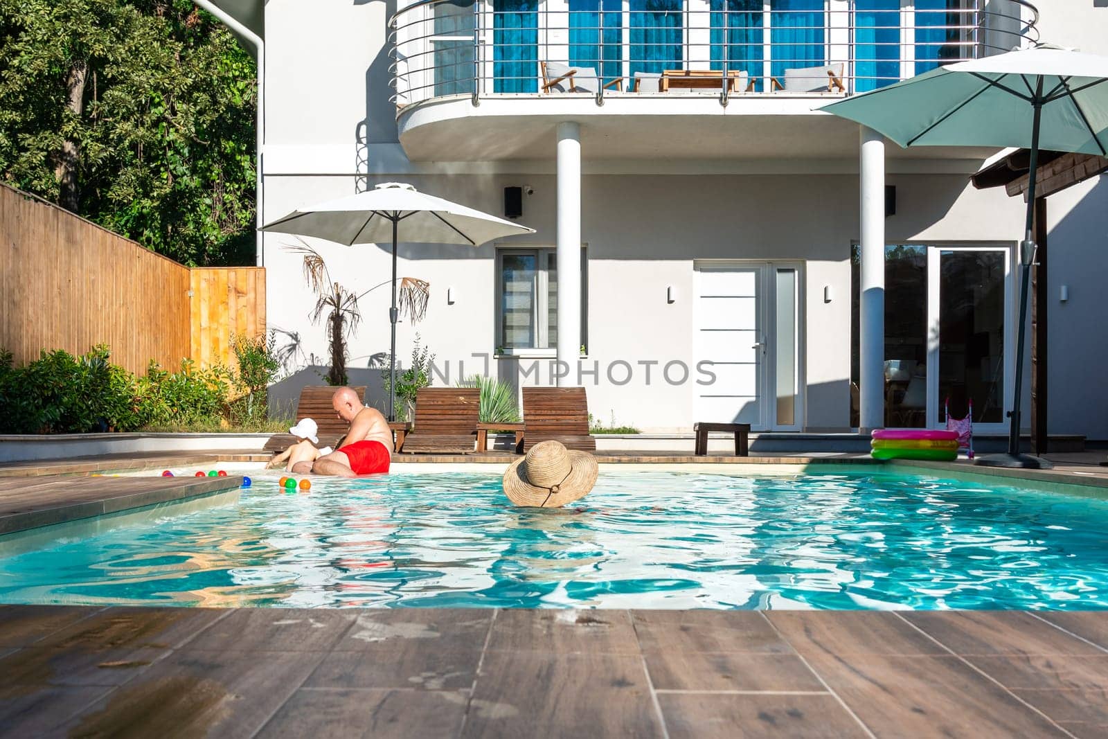 Family with young child enjoying a sunny day in the villa swimming pool, relaxing together. Concept of family bonding, leisure, and relaxation outdoors