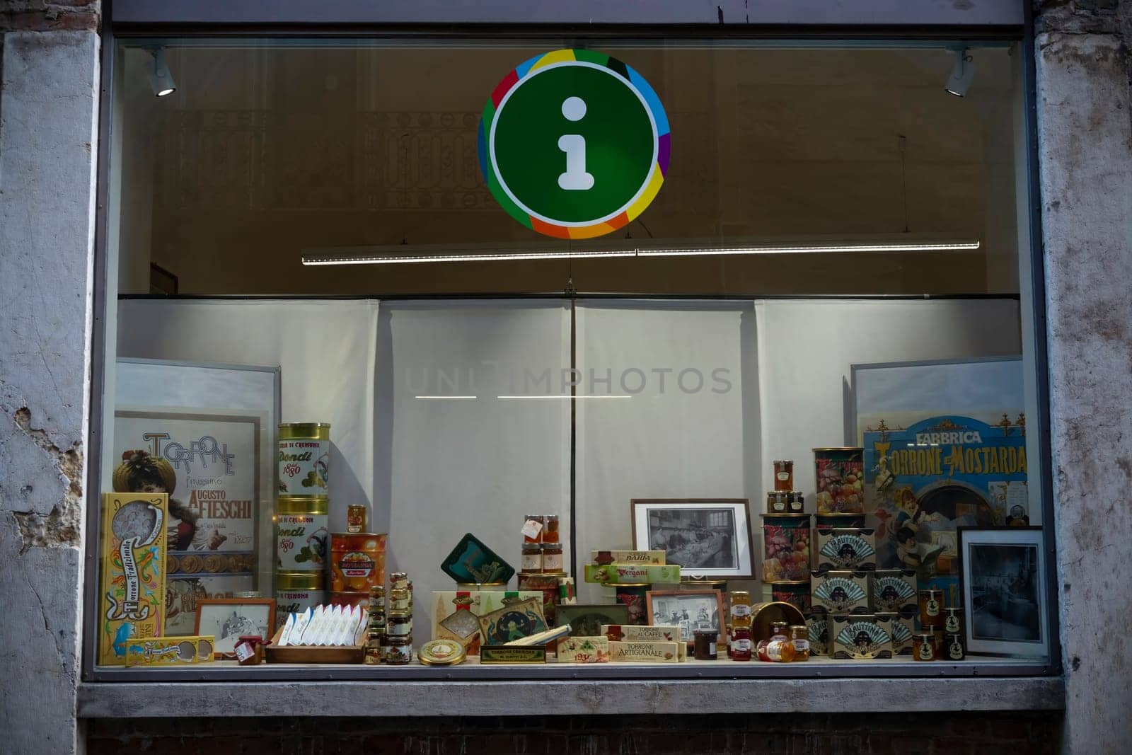 Cremona, Italy - November 27th 2024 Shop window in cremona, italy, showcasing local products and vintage advertising posters, with a prominent tourist information sign