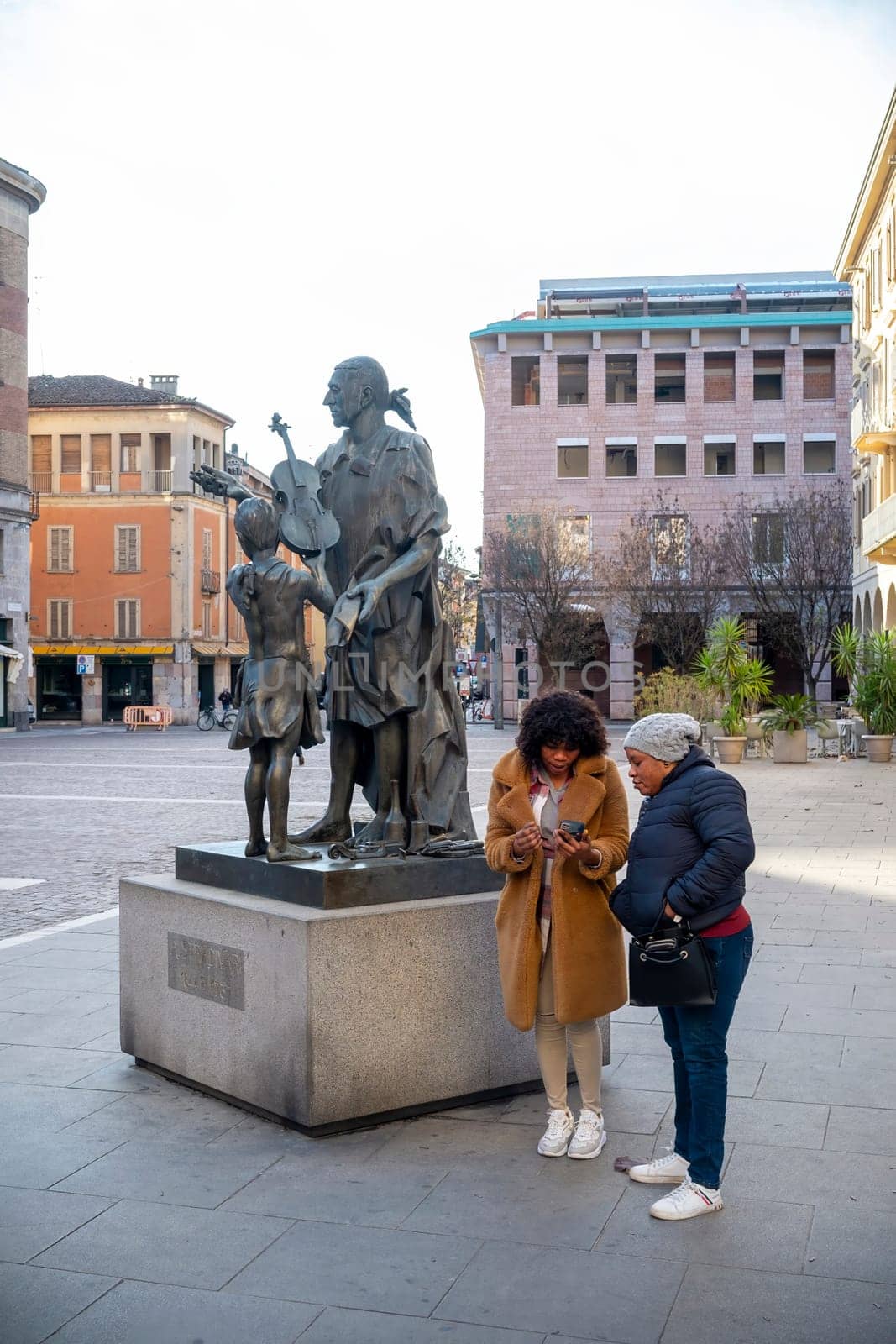 Cremona, Italy - November 27th 2024 Two tourists are using a smartphone near the monument to antonio stradivari, the famous violin maker, in cremona, italy