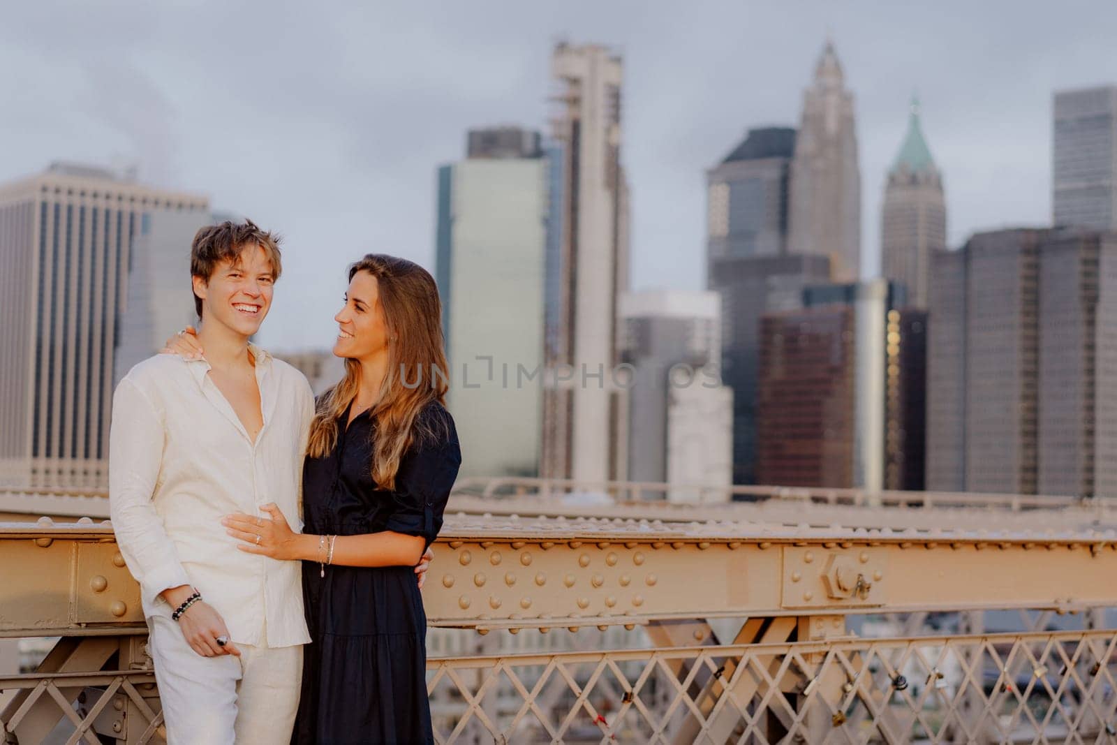 A lovely couple shares a sweet, tender kiss on the iconic Brooklyn Bridge, with the stunning NYC skyline behind them
