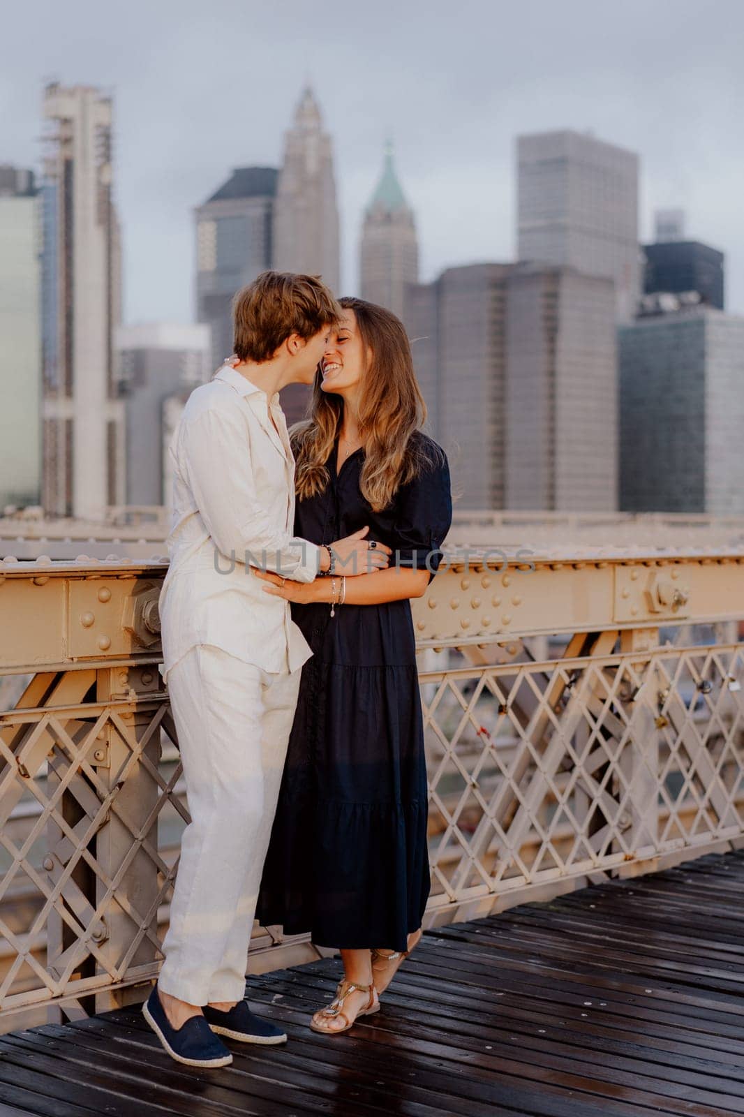A lovely couple shares a sweet, tender kiss on the iconic Brooklyn Bridge, with the stunning NYC skyline behind them