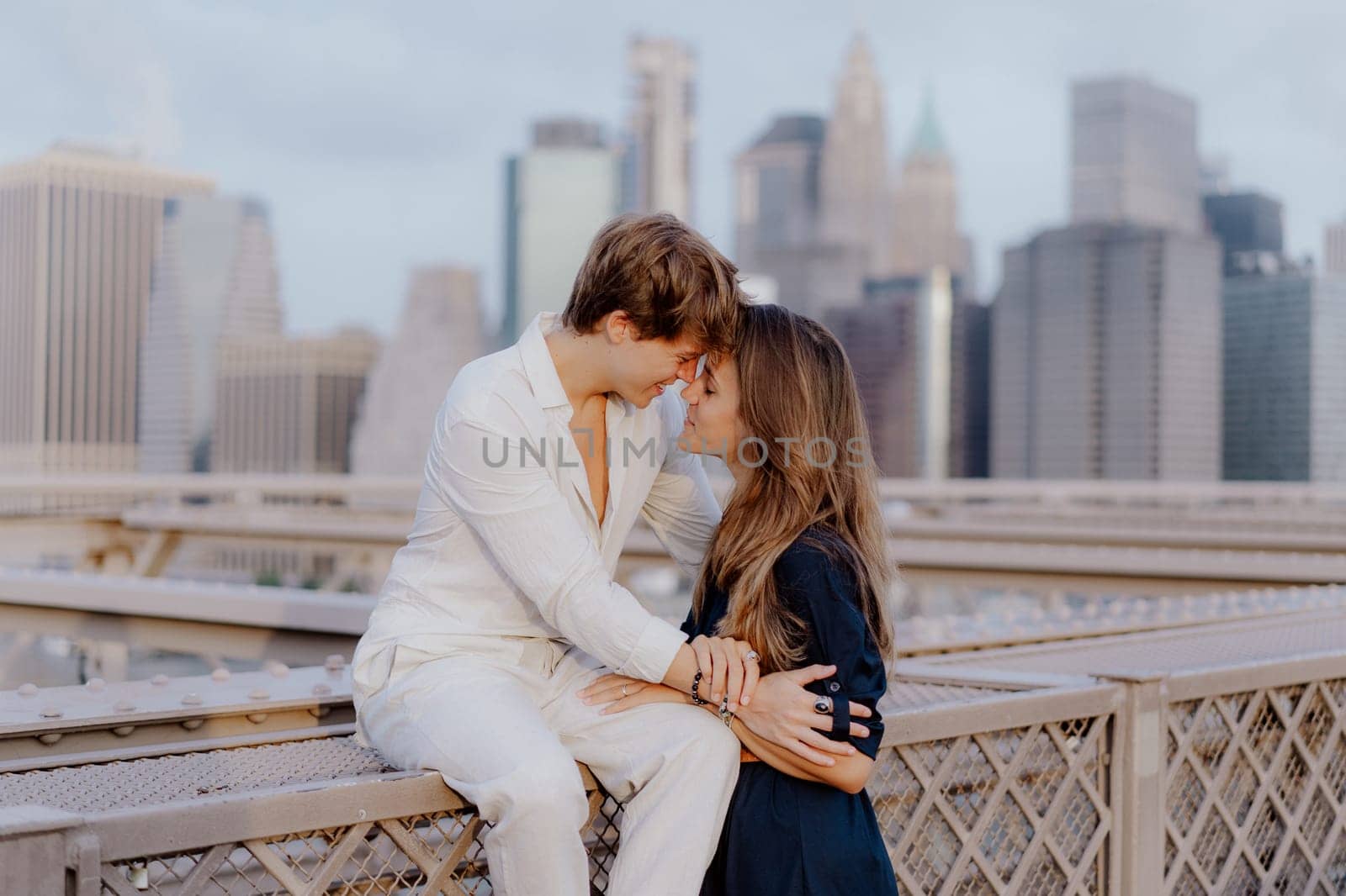 A lovely couple shares a sweet, tender kiss on the iconic Brooklyn Bridge, with the stunning NYC skyline behind them