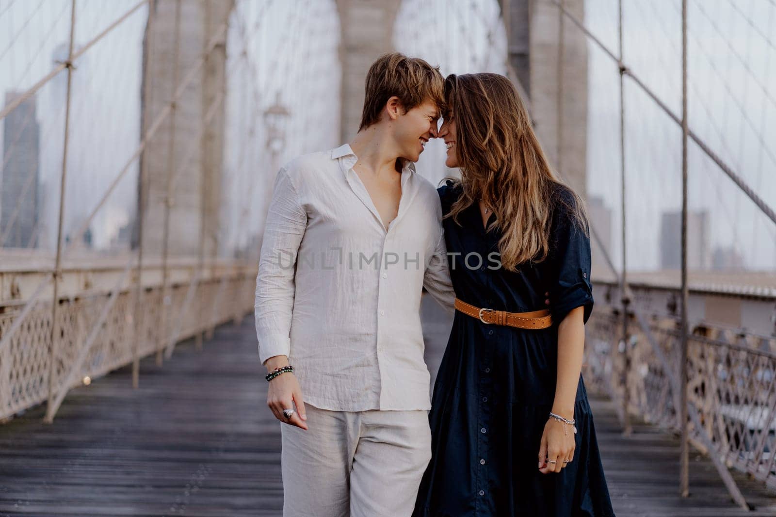 A couple strolls hand in hand on Brooklyn Bridge, surrounded by a stunning skyline and beautiful morning light