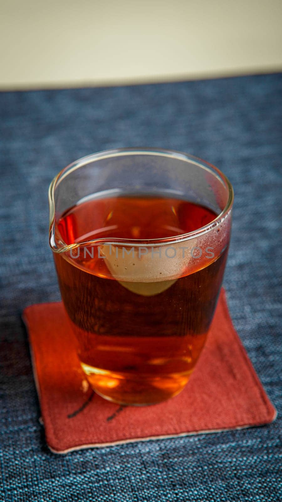 A beautifully crafted glass of fragrant tea is elegantly placed on a vibrant red coaster on a textured blue surface