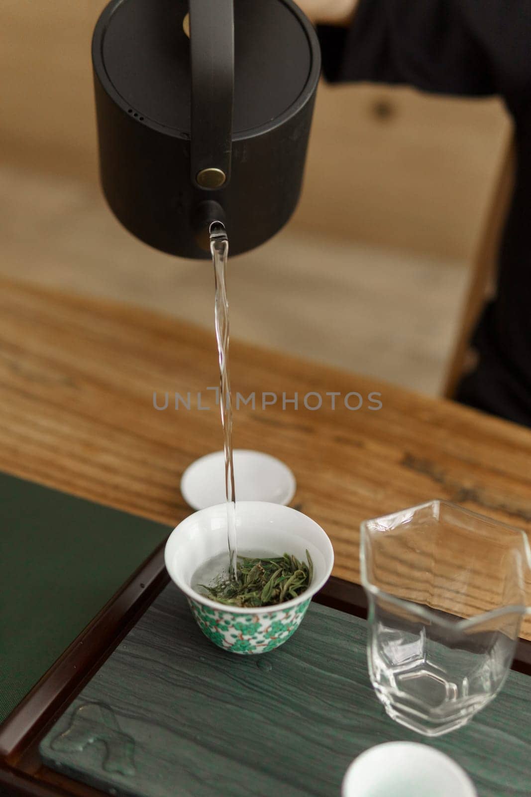 A serene and peaceful tea brewing process featuring a black kettle pouring hot water over fresh green tea leaves