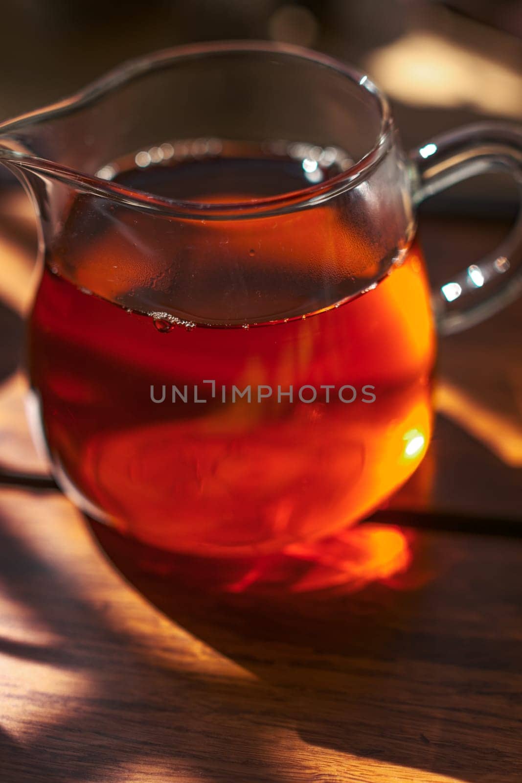 A beautiful glass teapot brims over with rich, aromatic amber tea, capturing the warm and inviting glow of sunlight