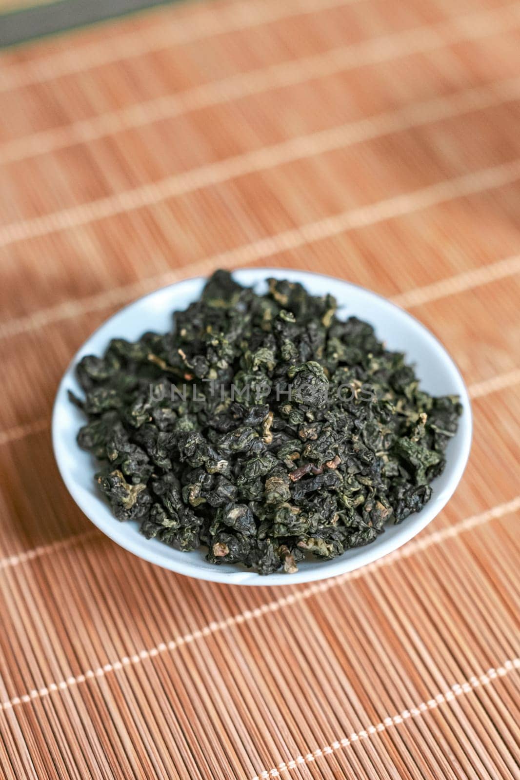 Closeup of dried green tea leaves arranged in a bowl, showcasing their vibrant color and intricate texture