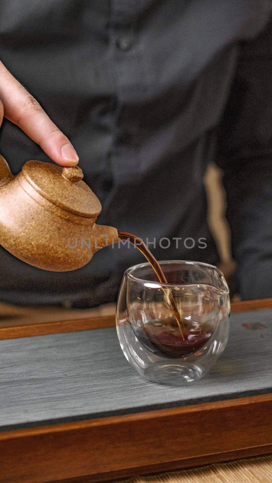 A skilled hand graciously pouring fragrant tea from an elegant traditional teapot into a clear glass cup