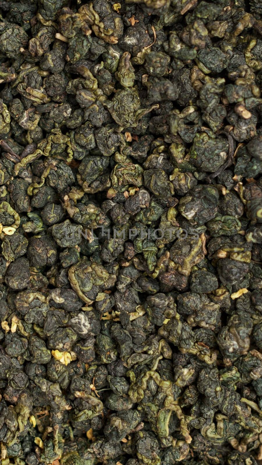 This is a detailed closeup view of dried green tea leaves, showcasing their unique texture and vibrant color
