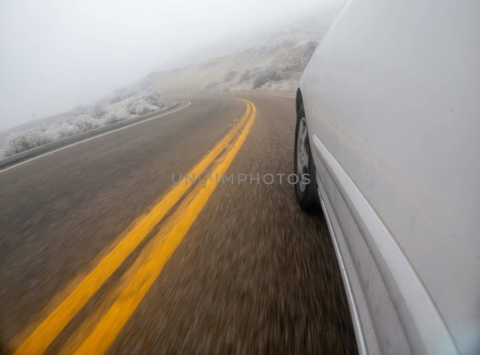 A car is driving down a road with yellow lines. The road is wet and the car is going fast