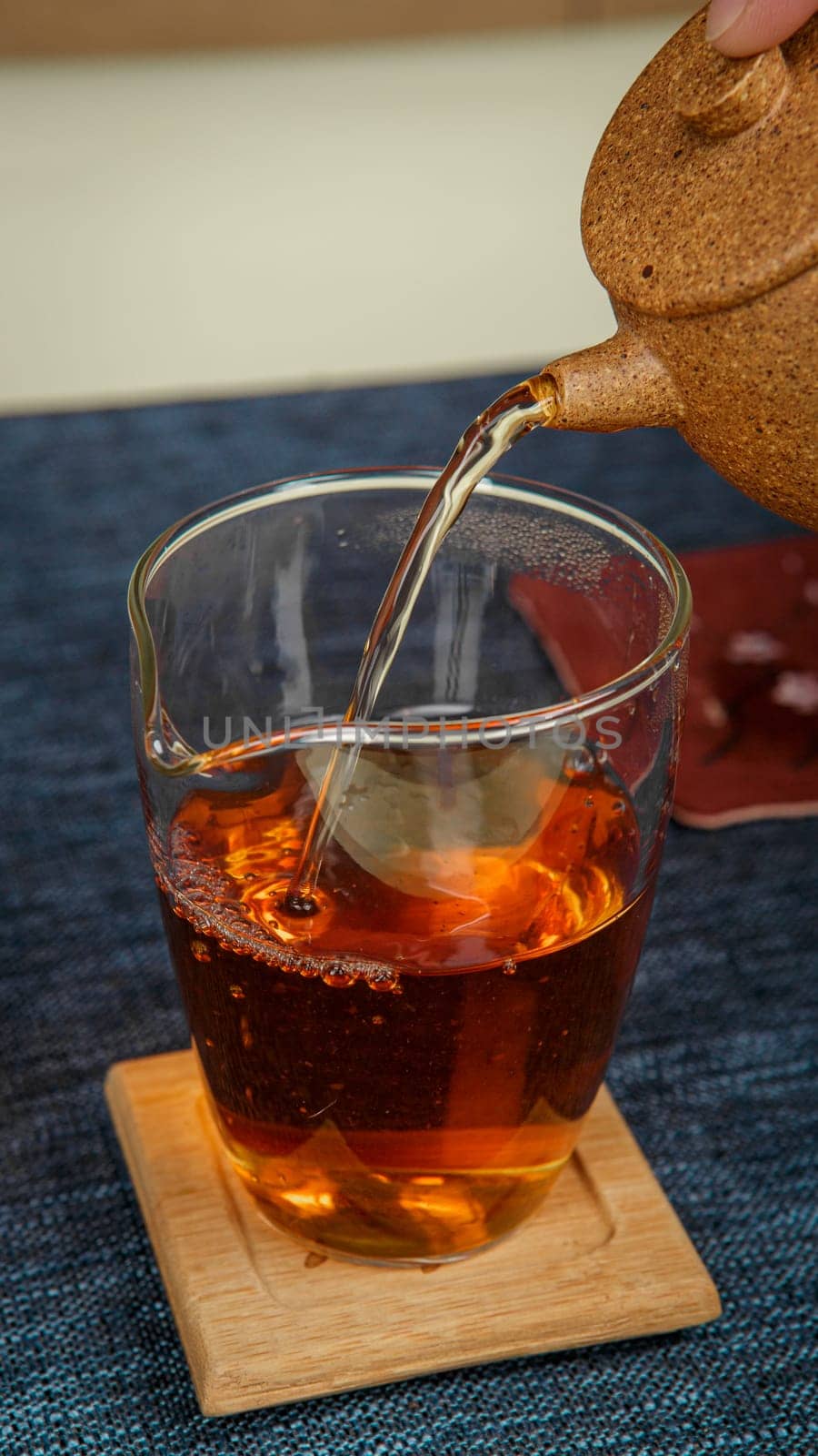 A serene moment of tea carefully being poured into a delicate glass cup that rests on a smooth wooden coaster