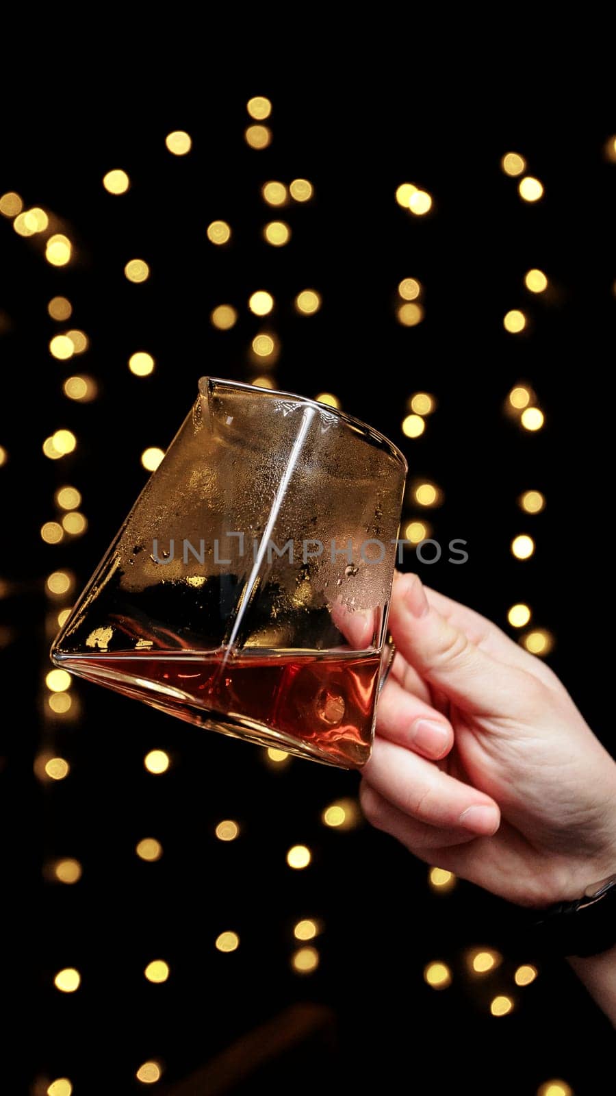 A hand holding a glass of rich liquor, surrounded by golden bokeh, creating a warm, inviting atmosphere