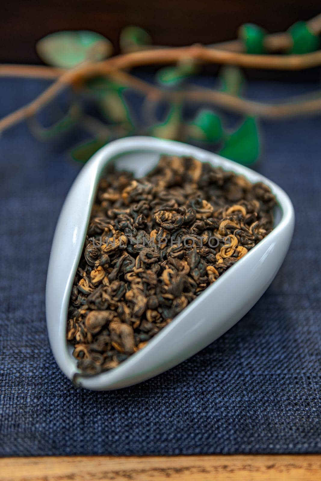 This presentation showcases dried herbal tea leaves elegantly arranged in a modern white dish on textured fabric