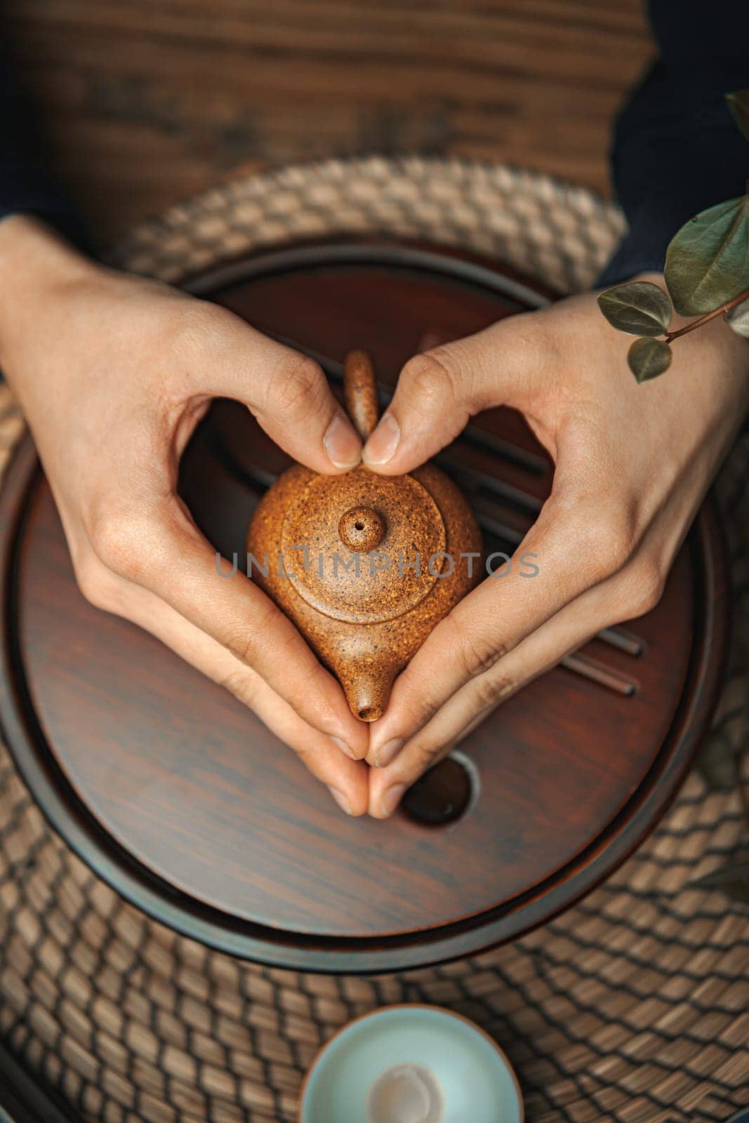 An imaginative display of hands graciously forming a heart shape around an exquisite teapot on a rustic wooden surface