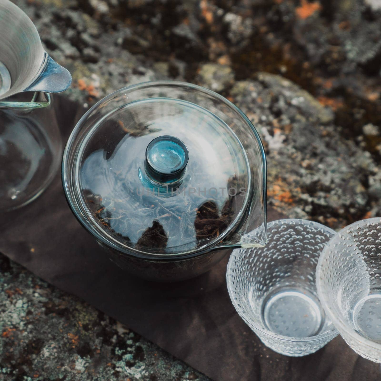 A beautifully styled tea setup showcasing an exquisite glass teapot alongside elegant cups placed atop textured stone
