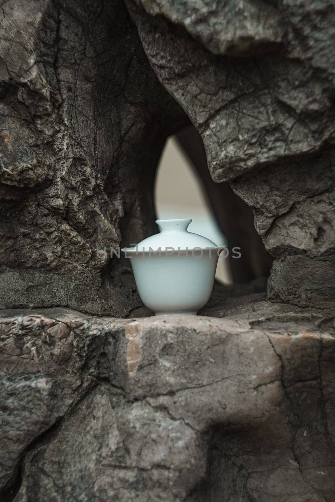 A delicate white teapot is positioned gracefully and elegantly within a rugged rocky formation in nature