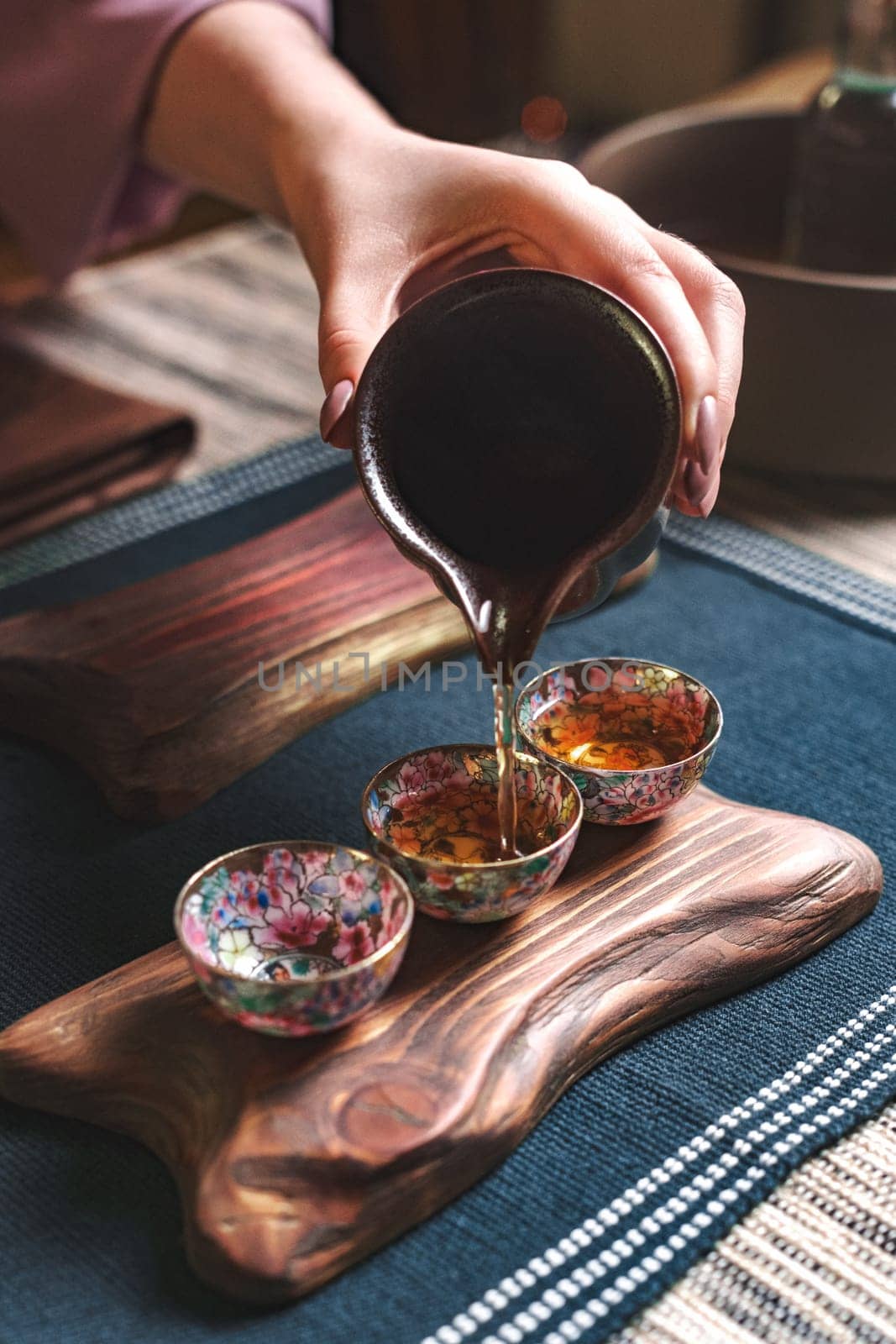 A hand pours aromatic tea into colorful cups on a charming wooden platter, showcasing a delightful drink experience