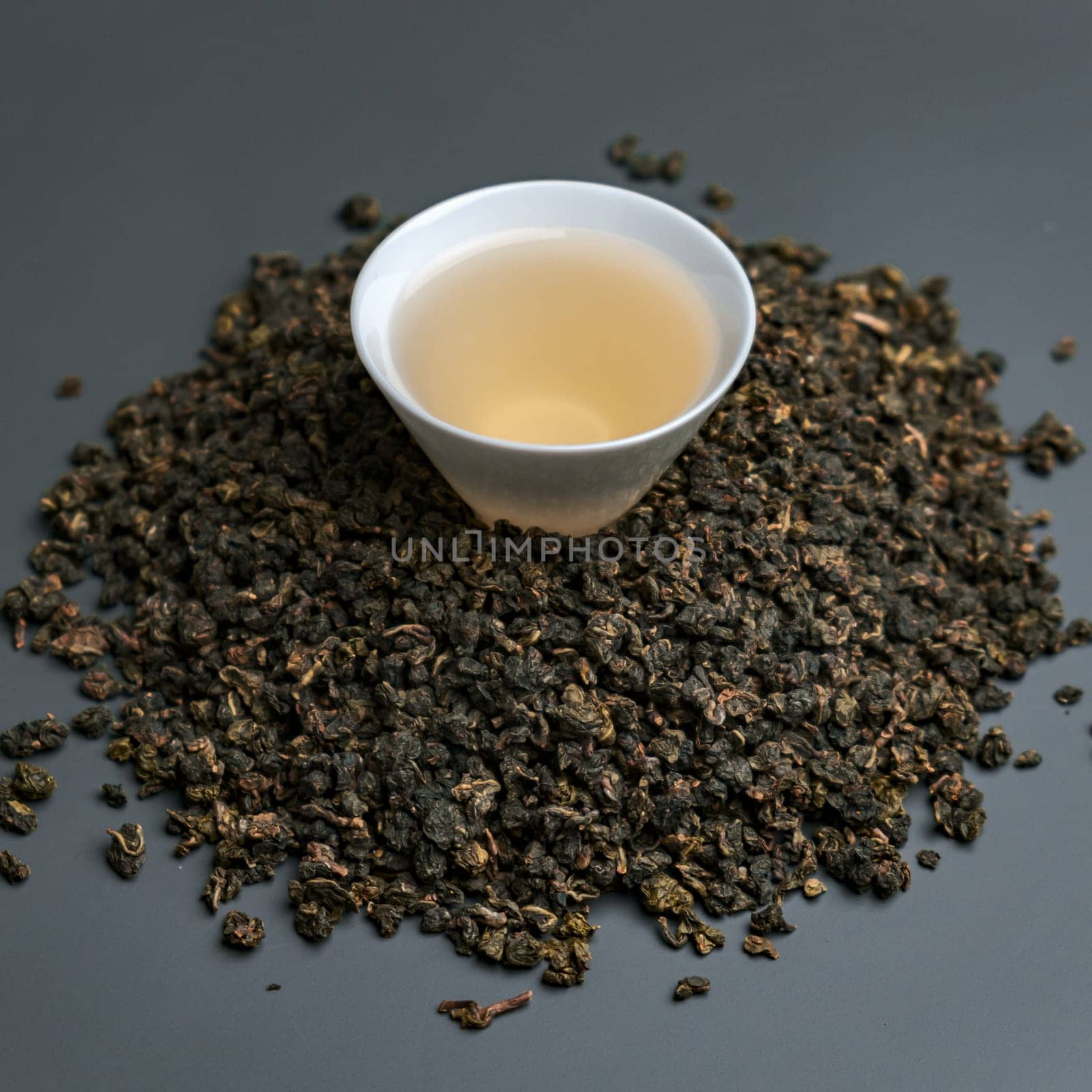 A detailed closeup view of beautifully arranged oolong tea leaves surrounding a warm cup of brewed tea