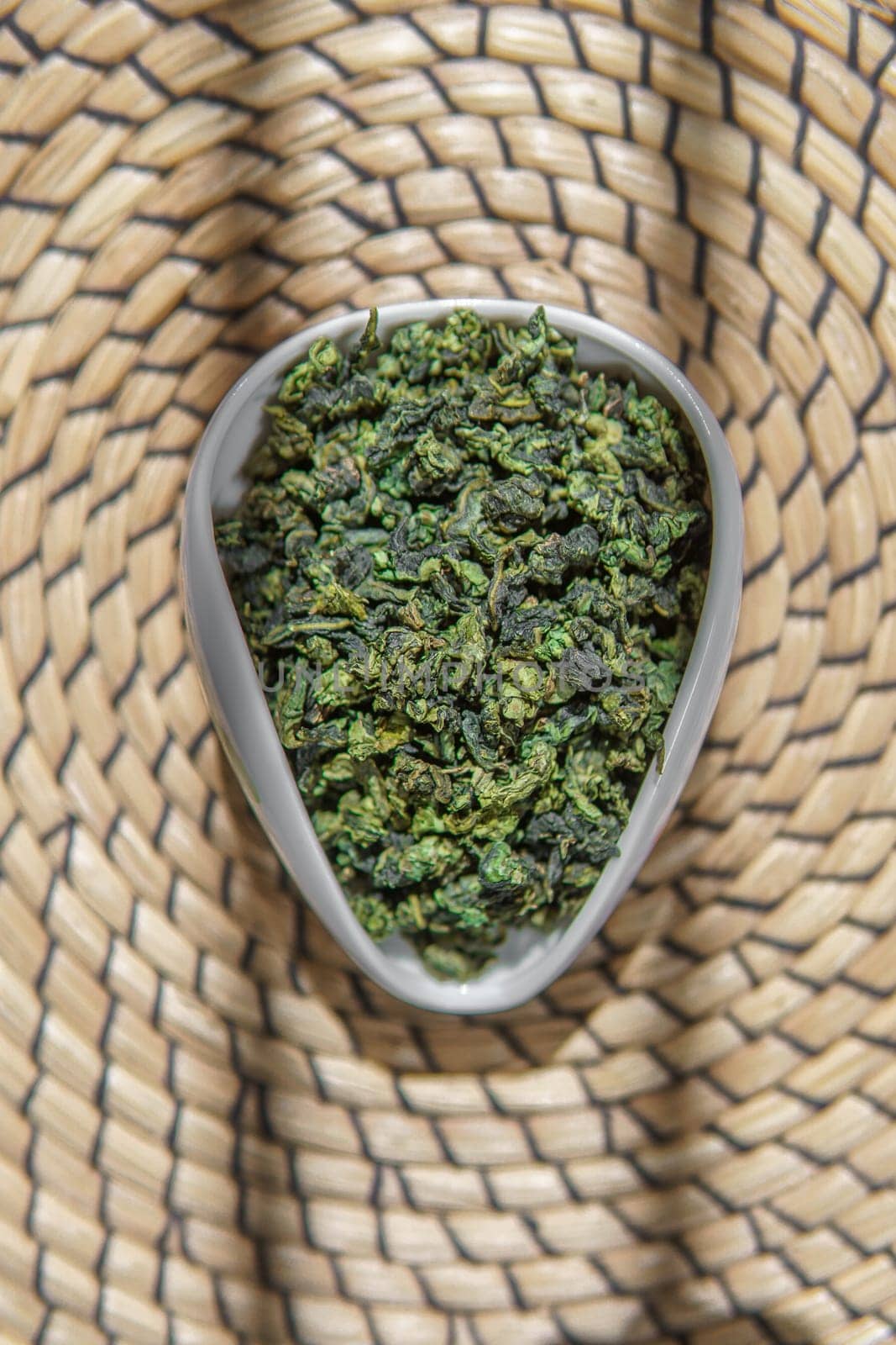 An aesthetic view showcasing dried green herbs beautifully arranged in a ceramic bowl placed on a decorative woven mat