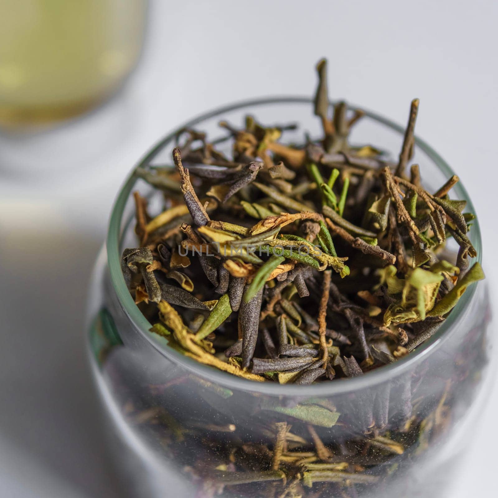 Closeup view of fresh green tea leaves beautifully arranged in a jar, with brewed tea elegantly blurred in background