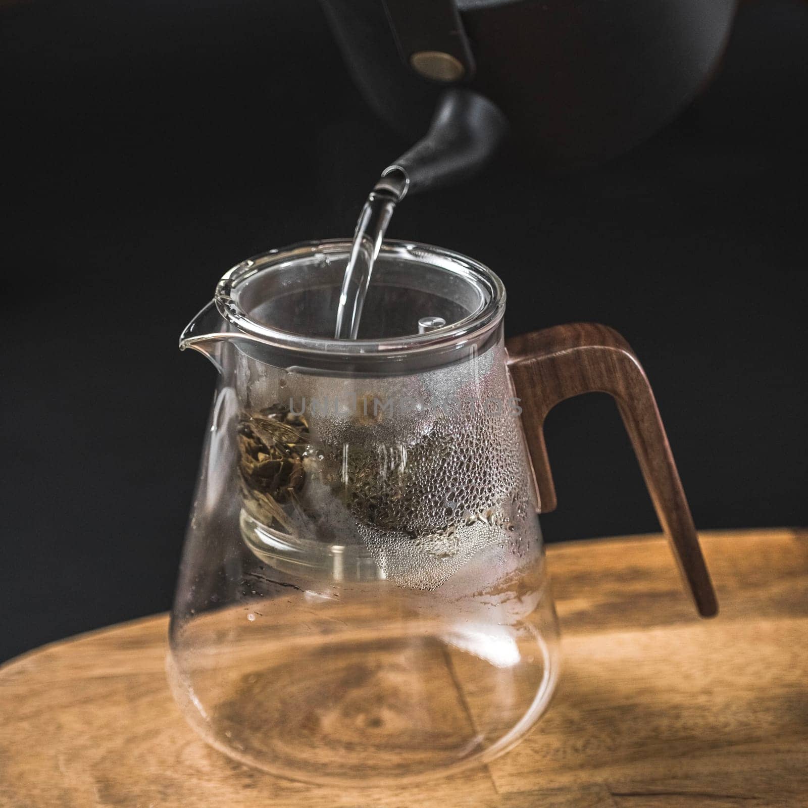 A stylish glass teapot pouring hot water for tea preparation, featuring a modern wooden handle design.