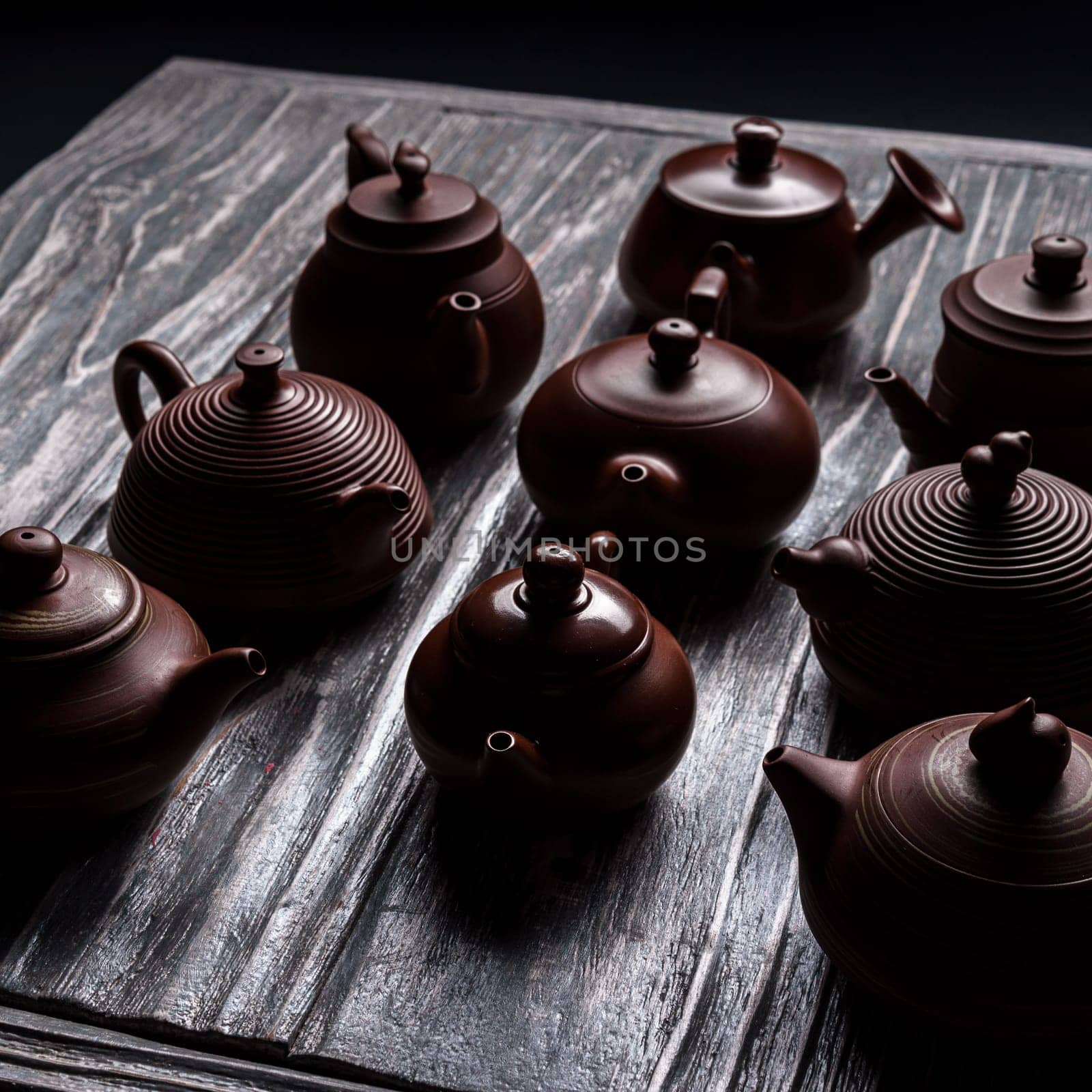 A striking and colorful display of various traditional teapots arranged on a beautifully textured wooden surface