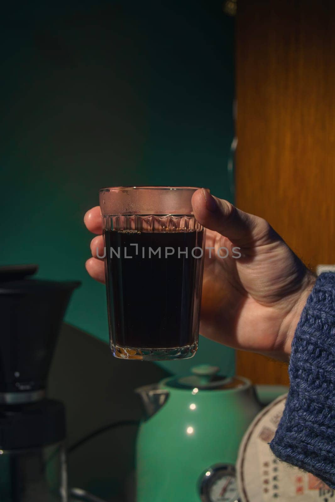 A cozy moment captured, focusing on a hand holding a glass of dark beverage, perfect for coffee lovers