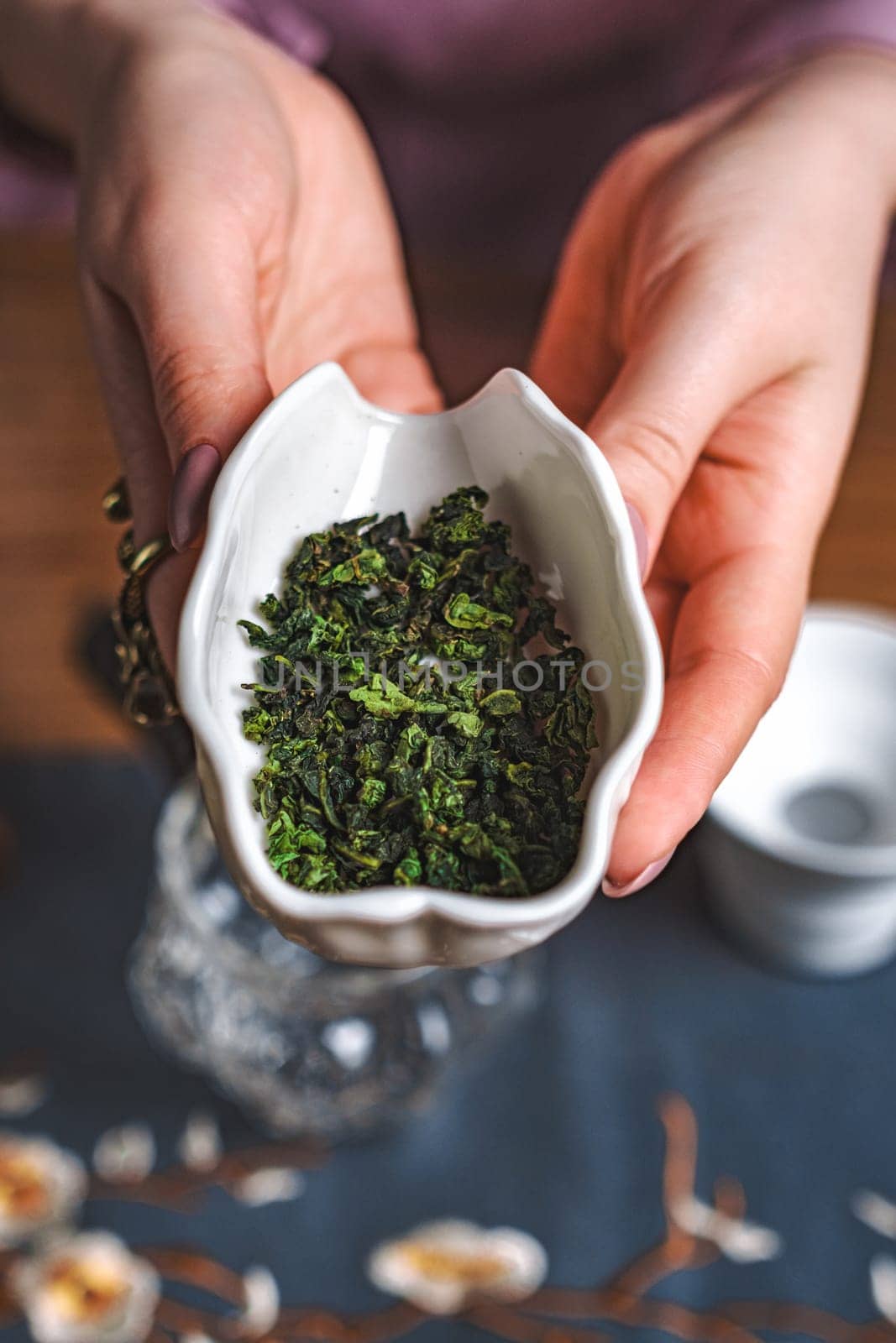 A hand cradles a crafted bowl filled with fresh green tea leaves, showcasing the essence of herbal goodness