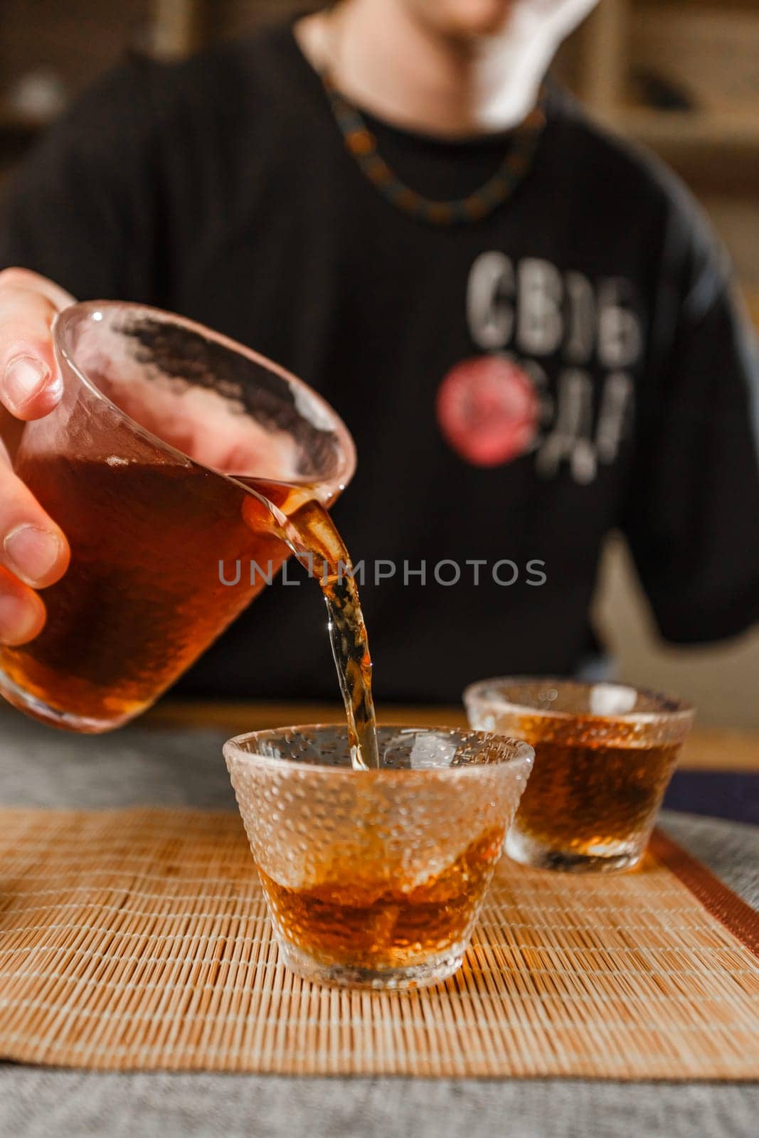 In a closeup shot, a hand gracefully pours a rich, dark beverage from a kettle into two elegant glass cups