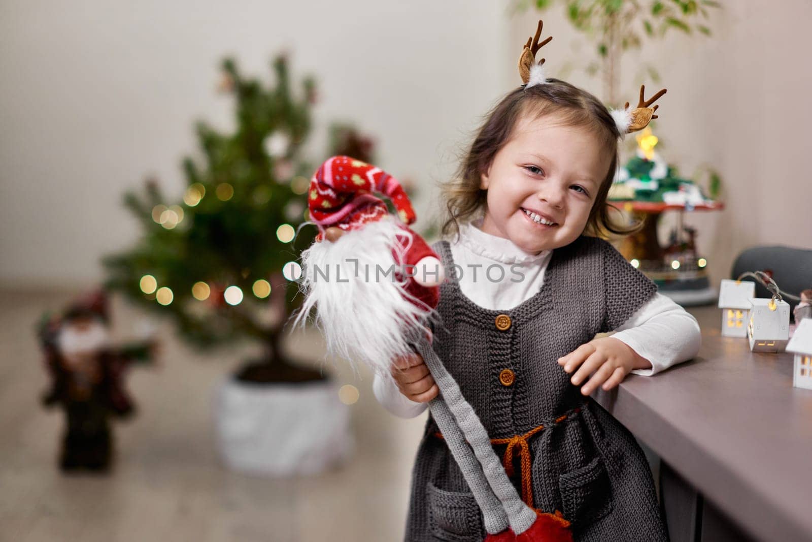 Cute smiling little child girl holding gnome near the Christmas tree at home