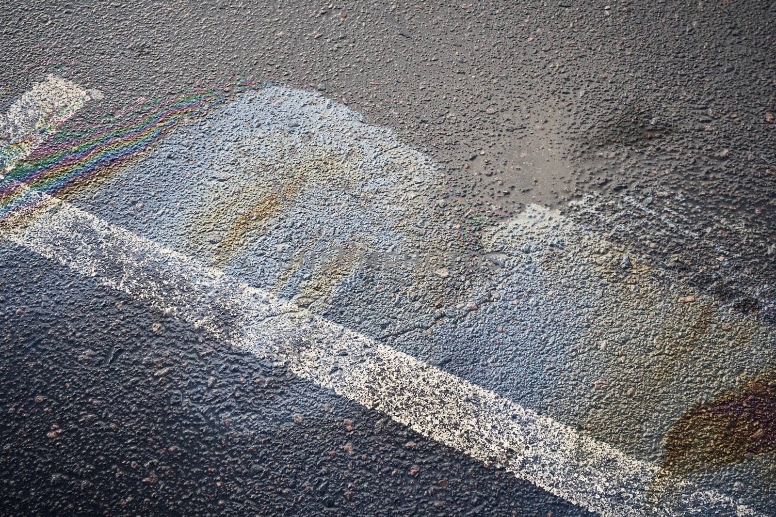 Gasoline or oil spill creating rainbow colors on wet asphalt road surface with white stripe.
