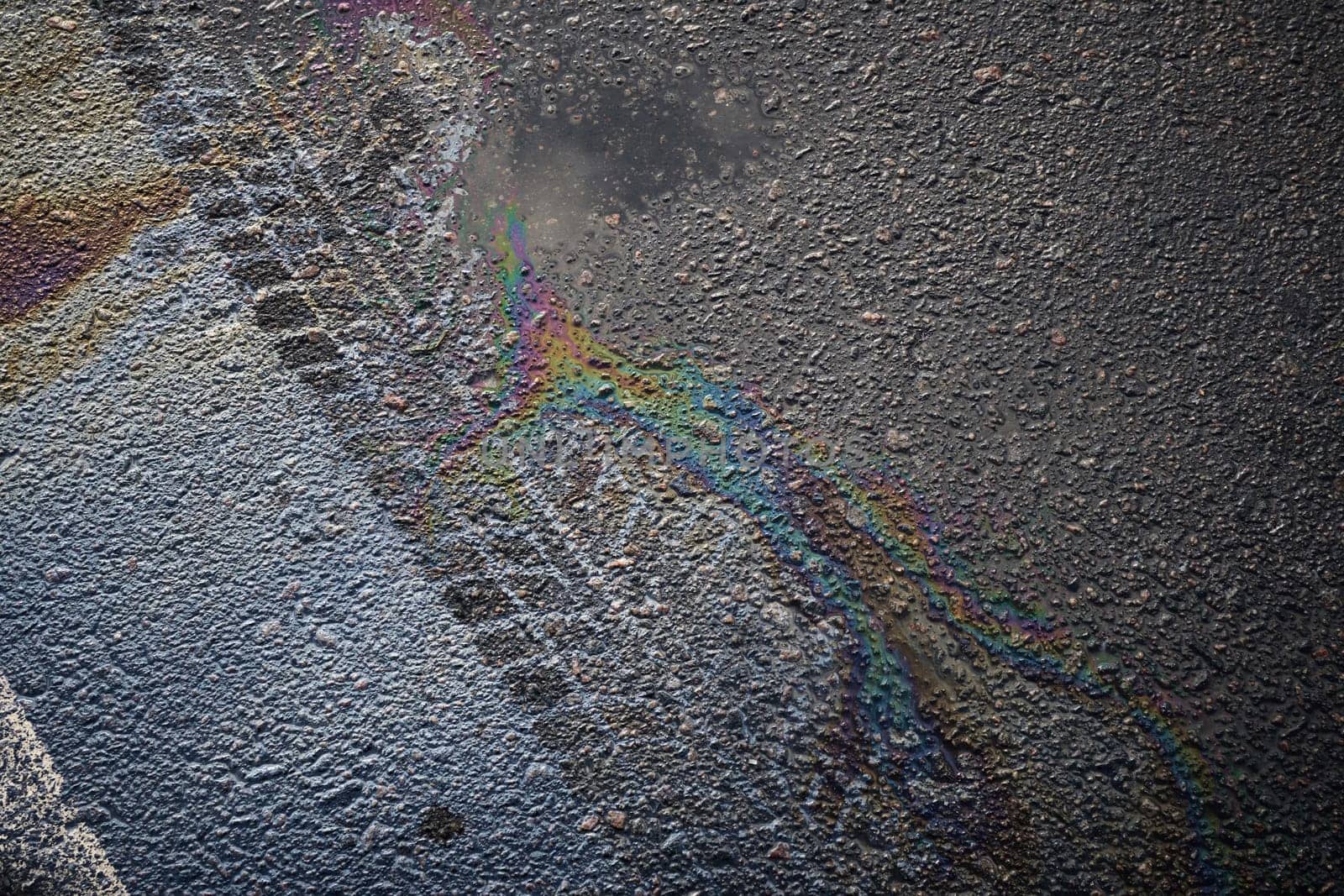 Close-up of tire marks and gasoline or oil spill creating a rainbow effect on wet asphalt road surface.