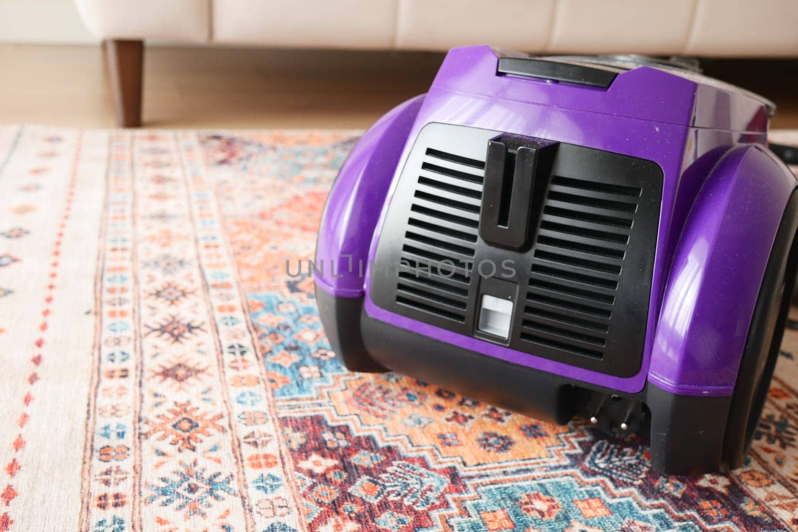 A vibrant and eyecatching purple vacuum cleaner is placed on an intricate vintage rug