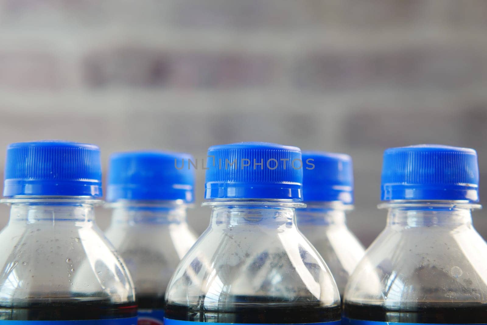 A collection of bottled drinks with blue caps against a textured brick backdrop.