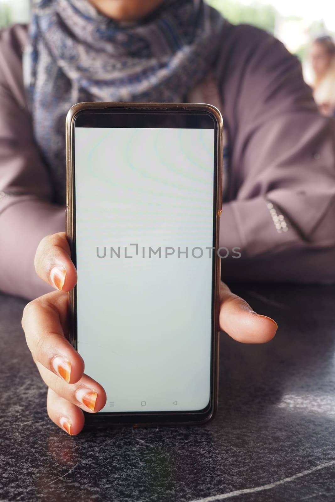 In a cozy cafe setting, an individual is showing off a smartphone that has a blank screen