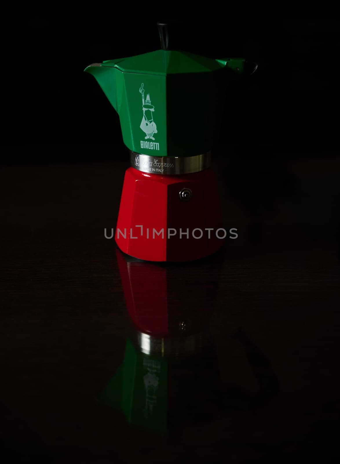 Italian espresso maker in green and red with a striking reflection on a dark surface, capturing a classic kitchen theme.