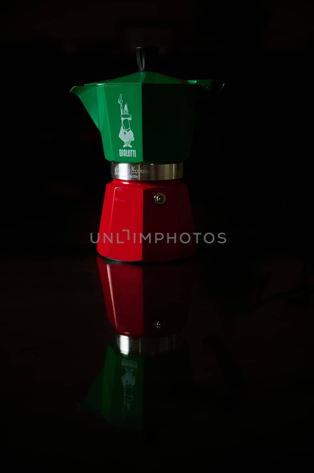 A red and green espresso coffee maker displayed on a reflective surface, enhancing its colorful design.