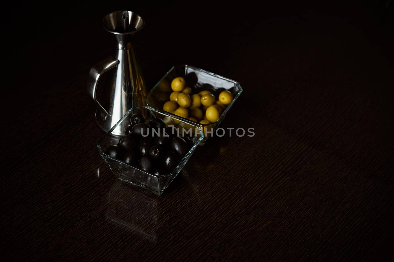 A sophisticated arrangement of green and black olives with an oil dispenser, highlighting culinary elegance on a dark table.