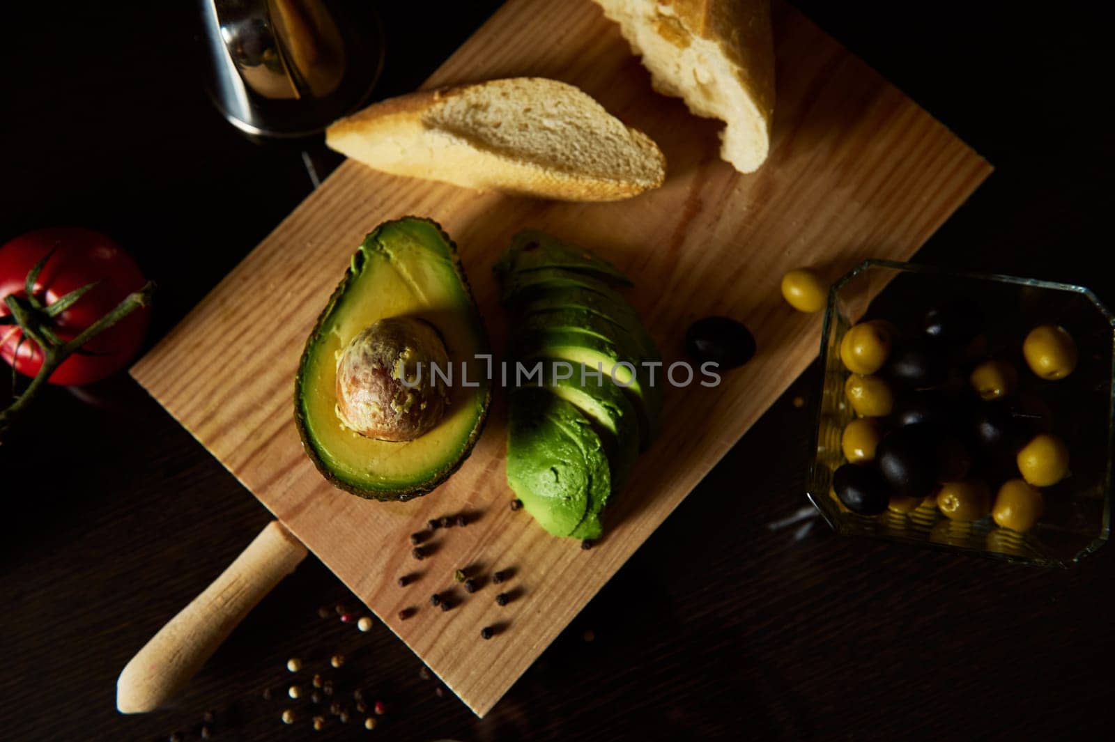 Sliced avocado with bread and olives arranged on a wooden board, creating a rustic and appetizing display. Perfect for recipes, food blogs, or health-related content.