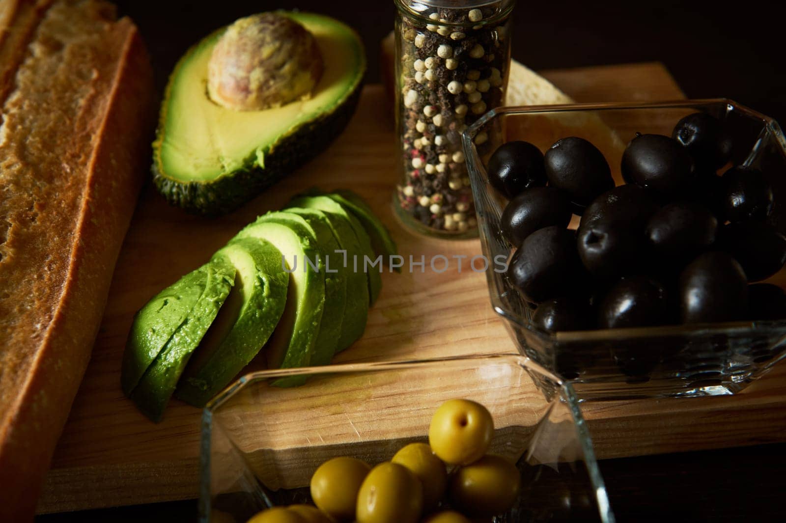 Close-up of fresh avocado slices, black and green olives, bread, and spices. Perfect for healthy eating concepts and Mediterranean cuisine inspiration.