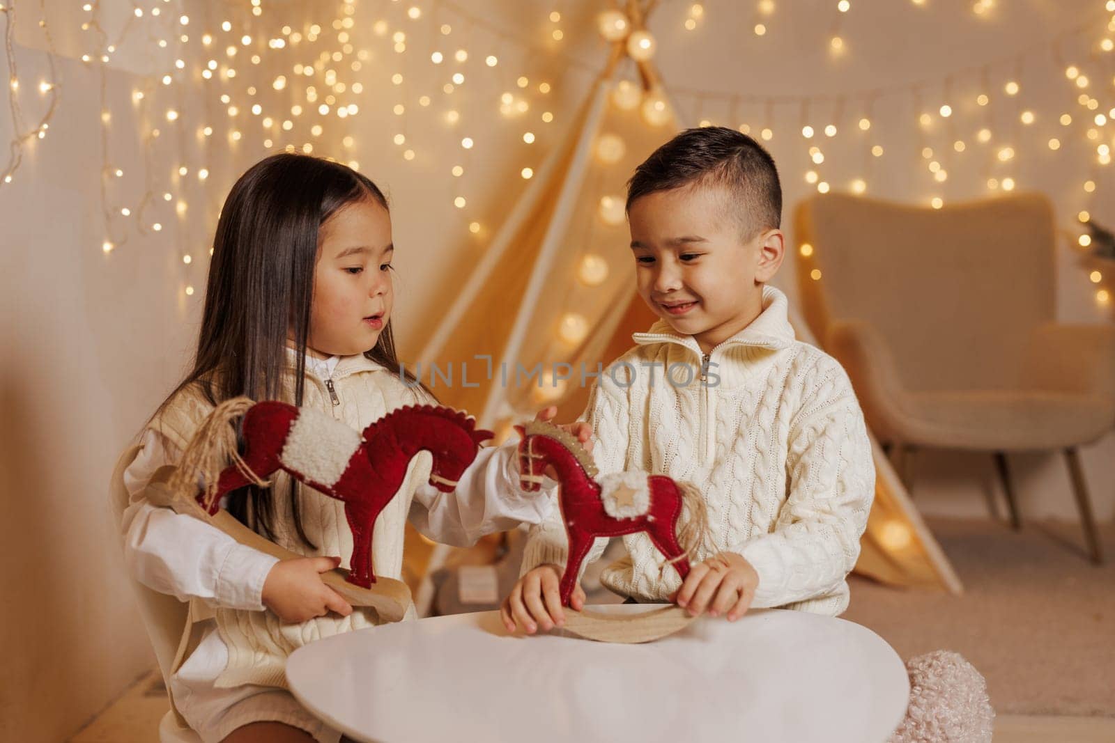 Two children playing with toy horses in a cozy room decorated with Christmas lights. children's room