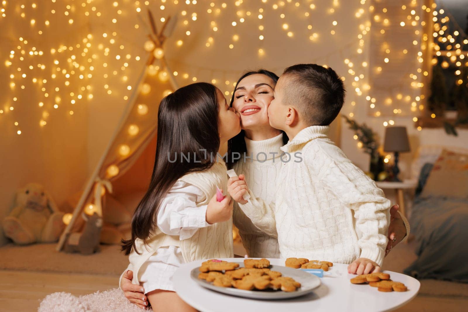 two children kissing mother on christmas evening in cozy room, happy family on christmas,
