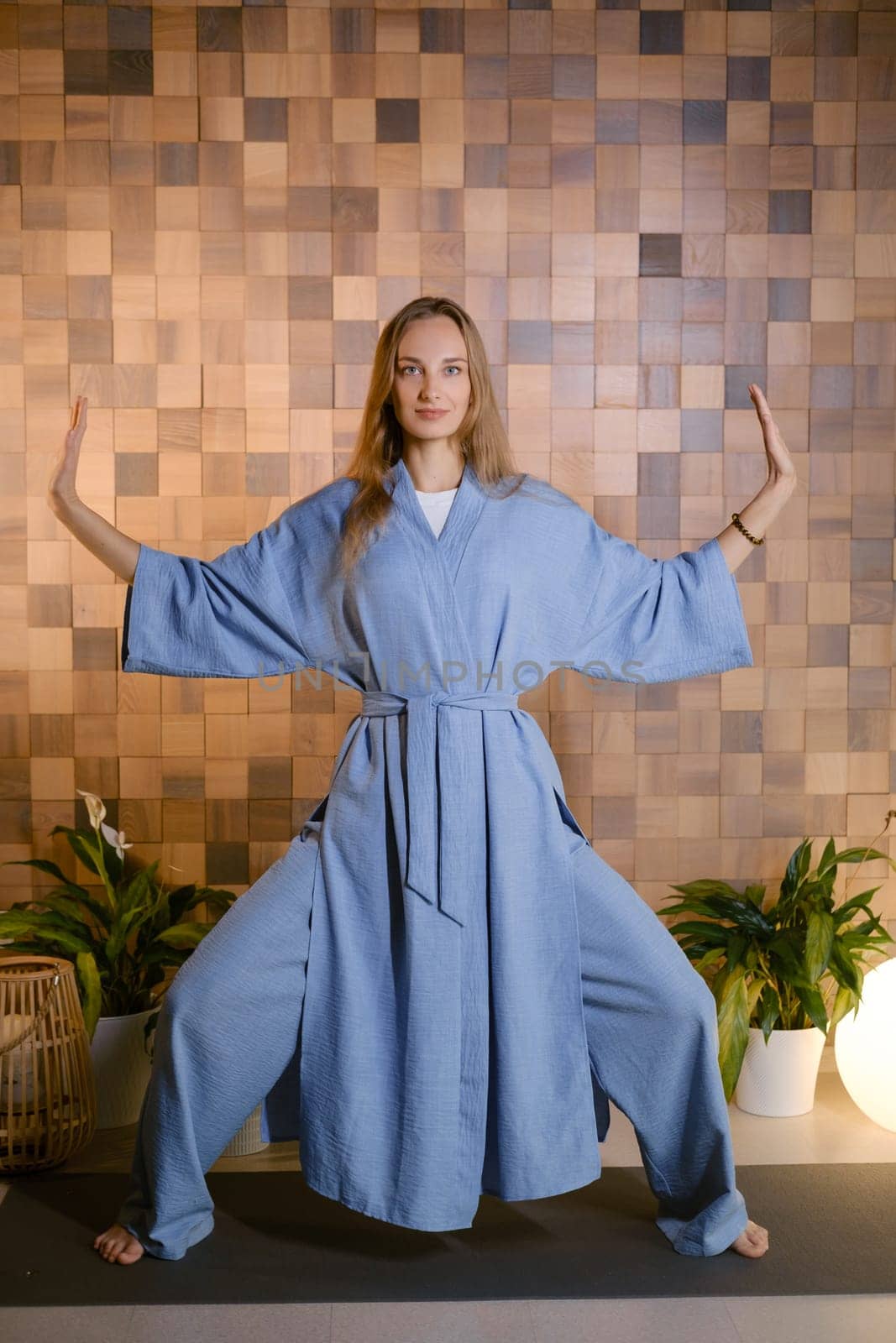 Yoga instructor in blue kimano at fitness gym . The girl does qigong yoga. The exercises are based on the movement of internal energy, the system of channels, energy centers, chakras.