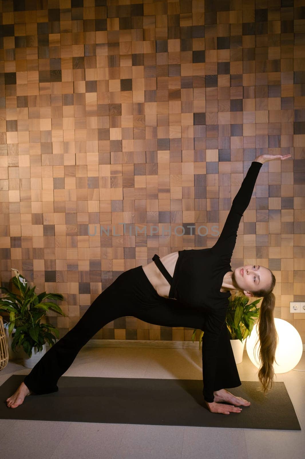 Slender attractive girl in black sportswear doing yoga in fitness room.