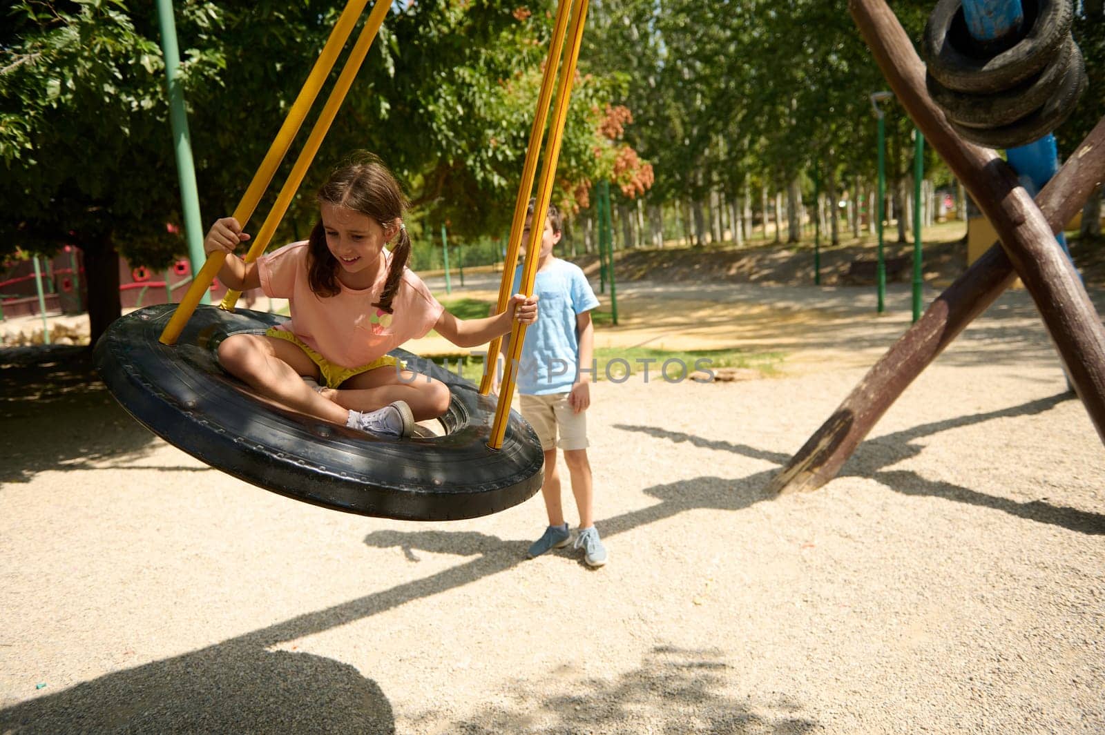 A young girl joyfully swings on a tire swing at a sunny park, enjoying outdoor fun.