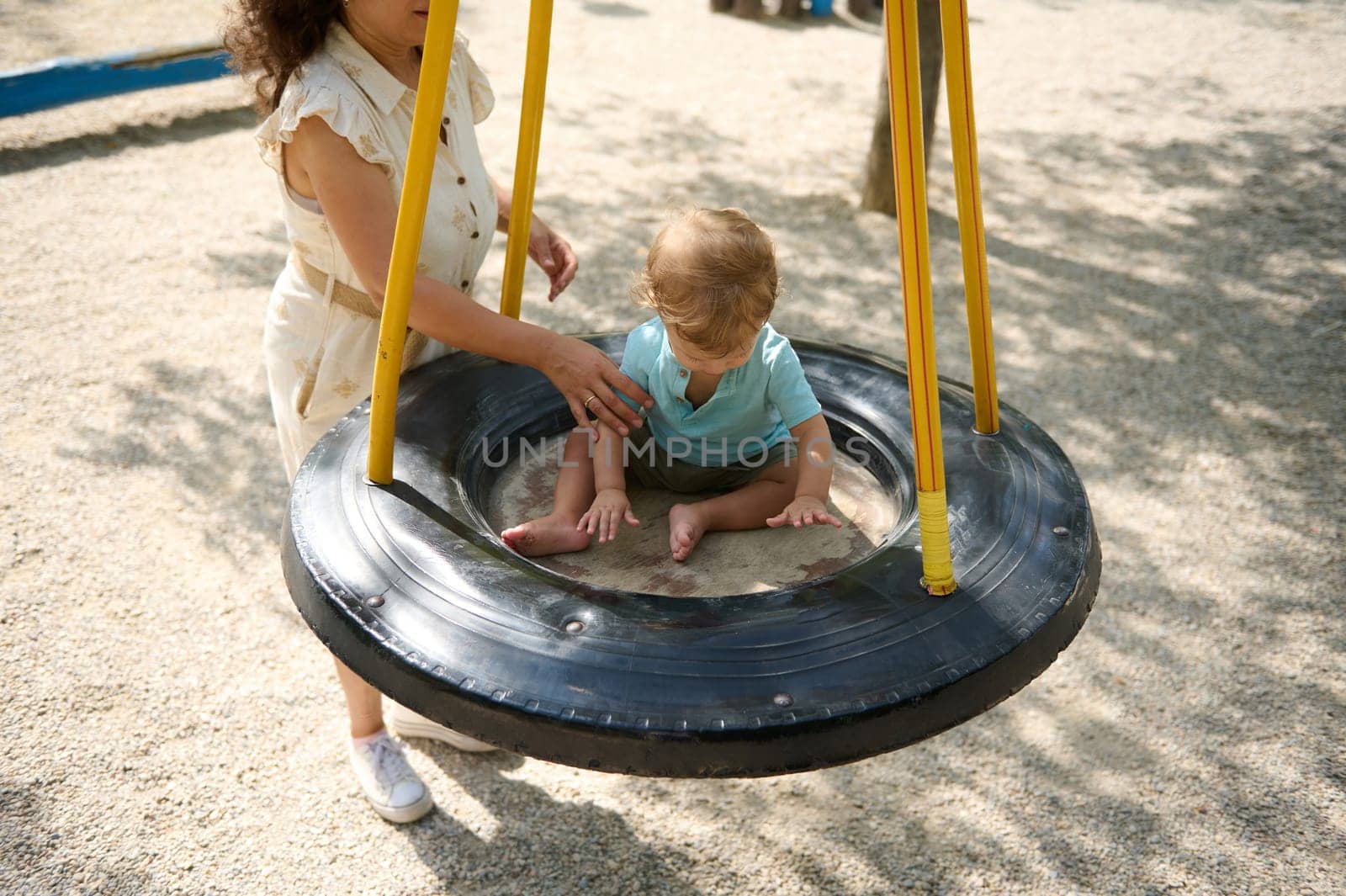 A mother assists her young child on a tire swing during a sunny day at the playground, fostering bonding and joy in a beautiful outdoor setting.