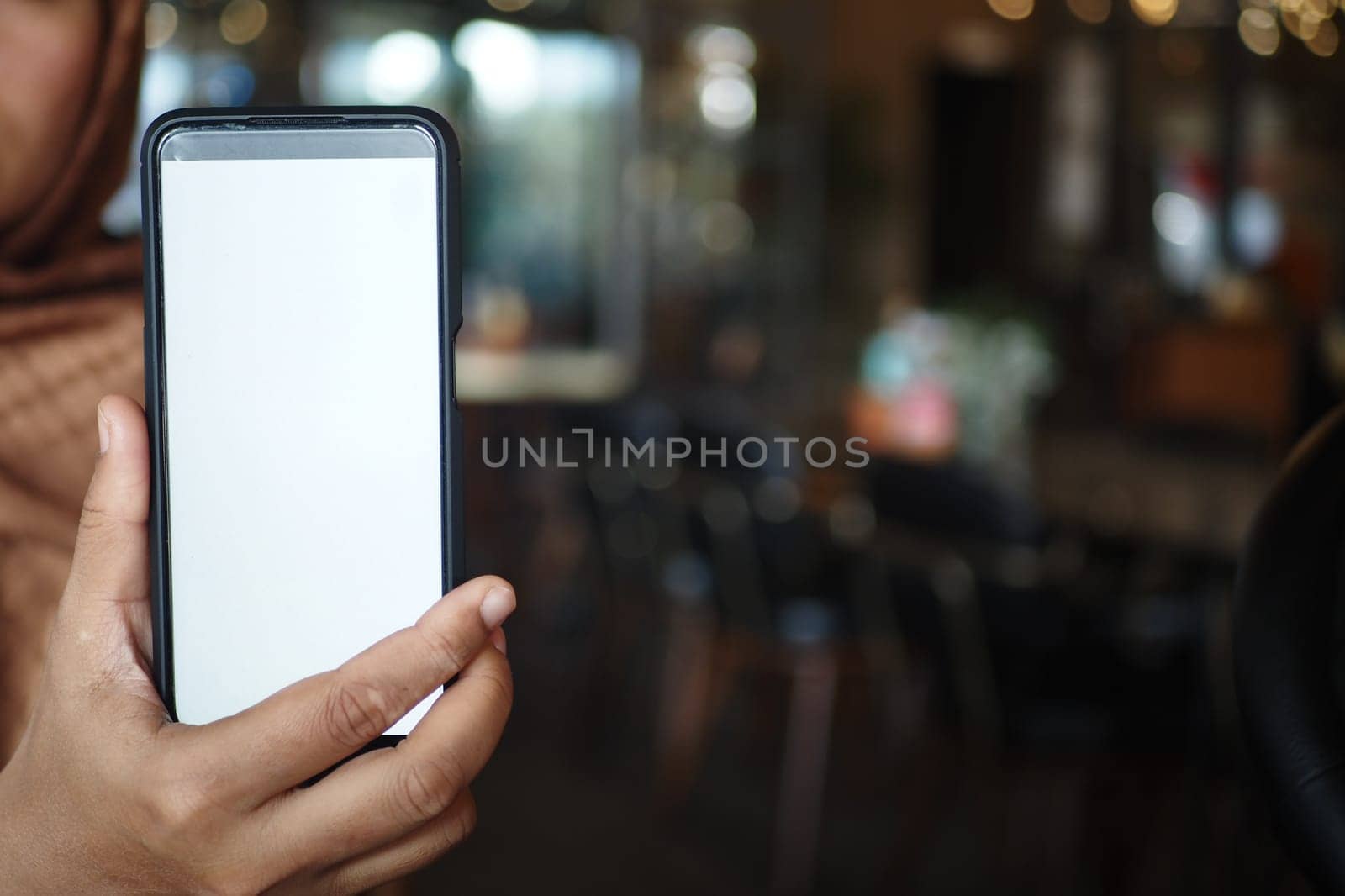 In a cozy cafe, a person holds a smartphone with a blank screen, reflecting stillness